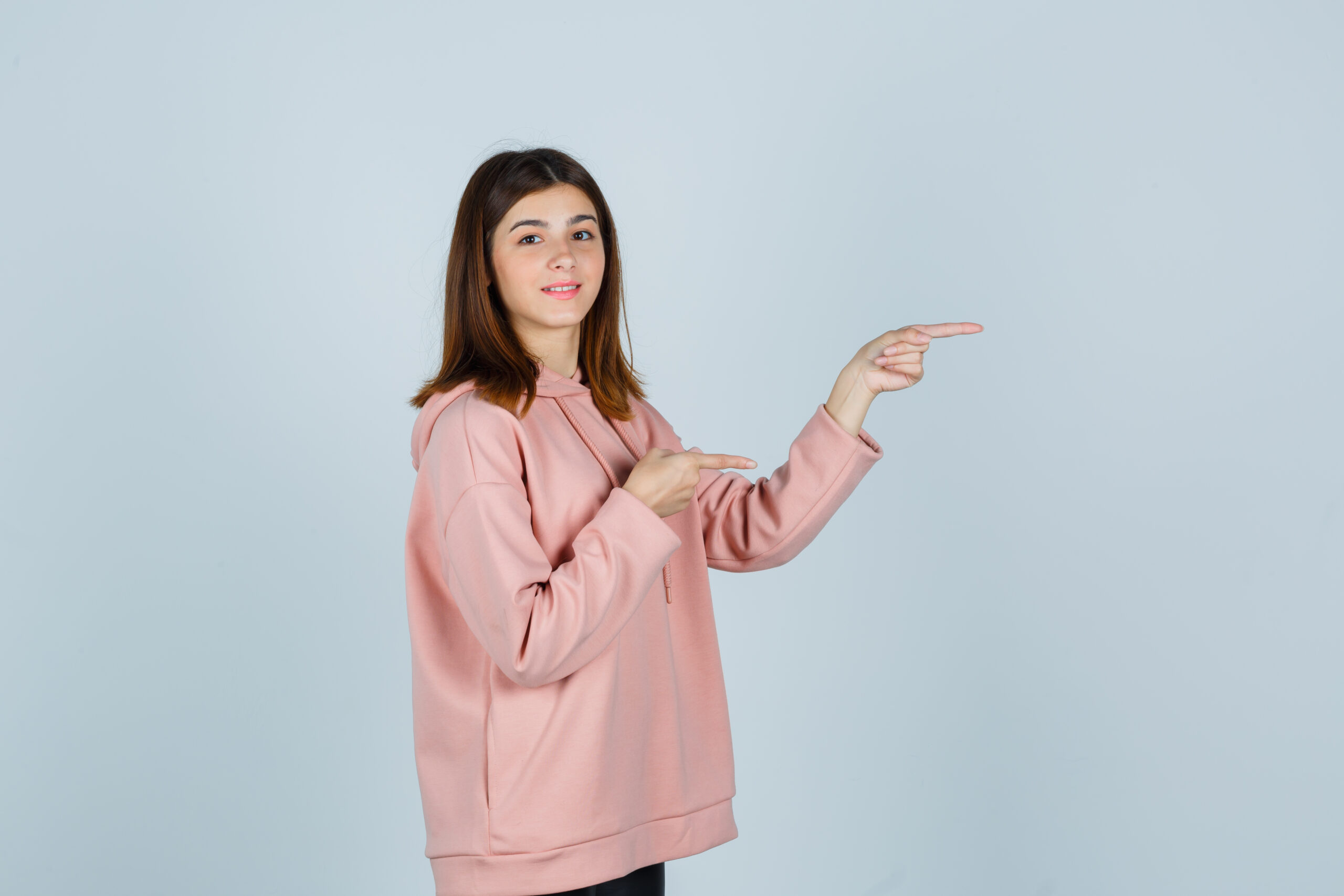 young lady pointing to the right side in oversized hoodie and looking confident , front view.