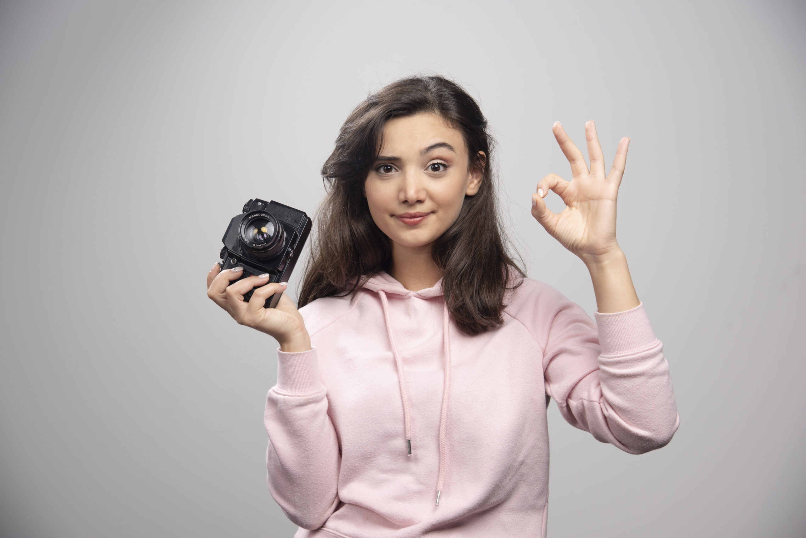 female photographer holding camera and making ok sign